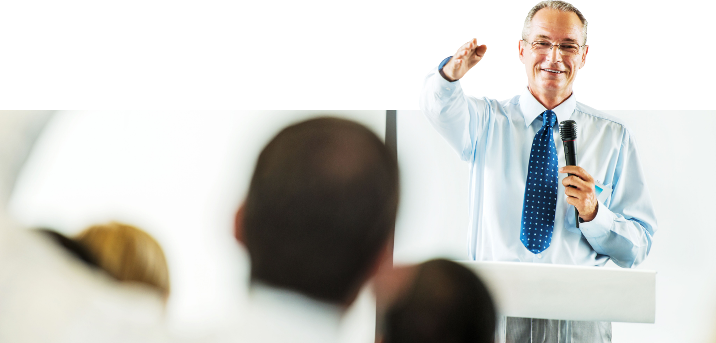 Man holding a microphone while giving a speech to an audience.