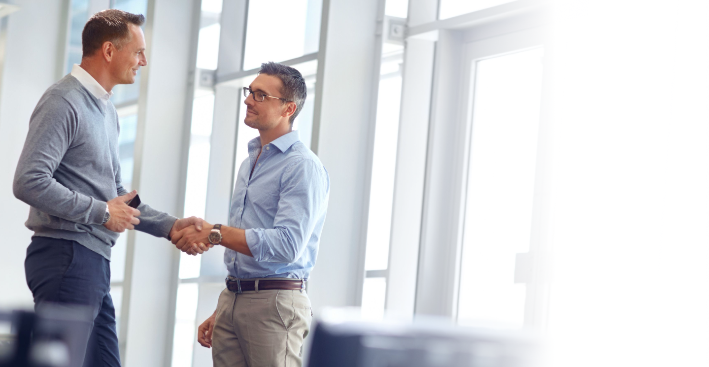 Two men shaking hands wearing semi casual business attire while in an office setting.