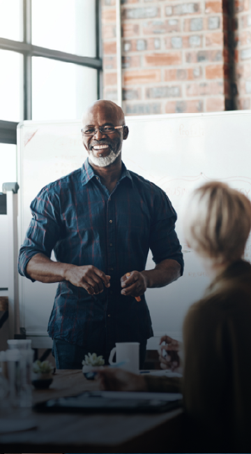 Man standing up in front of a whiteboard leading a meeting. 